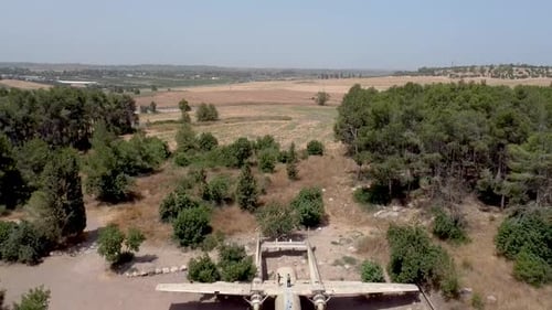 Aerial backwards drone shot above an old dismantled army plane monument placed on an empty dirt fiel