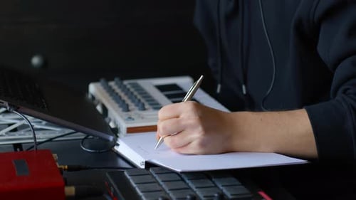 Close-up of music producer writing notes beside FX controller and MIDI keyboard