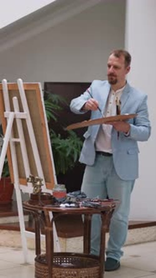 Artist Paints on Easel with Palette and Brush