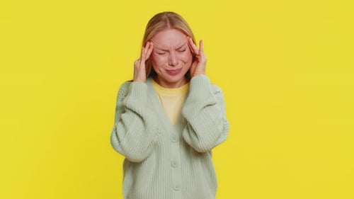 Woman Massaging Temples Experiencing Headache on Yellow Background