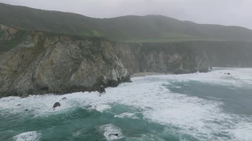 Aerial Slide and Pan Footage of Ocean Waves Rolling to Coast and Crashing to Rocks Haze Reducing