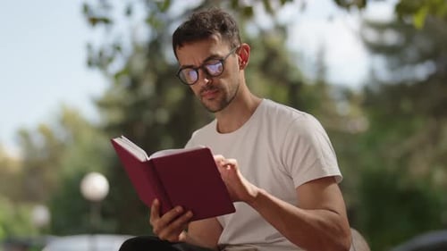 Junger Mann liest an einem Sommertag ein Buch auf einer Parkbank