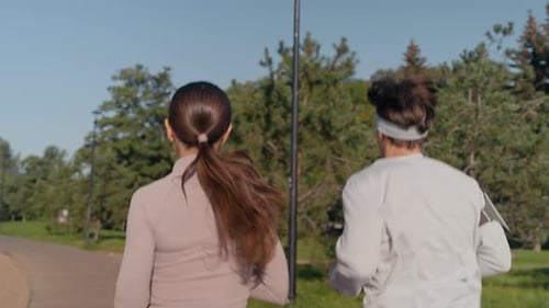 Rear View of Young Active Couple Jogging along Road in Public Park