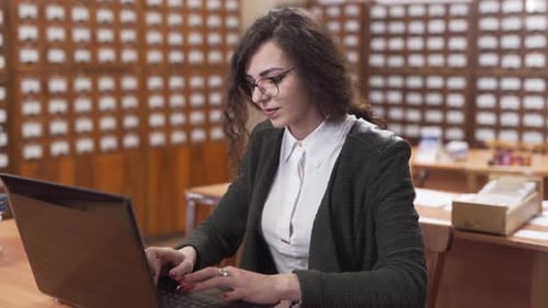 Lächelnde Studentin tippt auf ihrem Laptop an einem Holzschreibtisch in der Bibliothek.