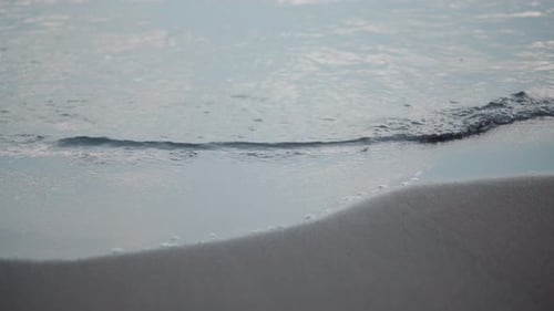 Ruhige Meereswelle, die am dunklen Sandstrand an Land geht