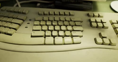 Old Dusty Keyboard Resting on a Cluttered Desk Filled with Tech Gadgets