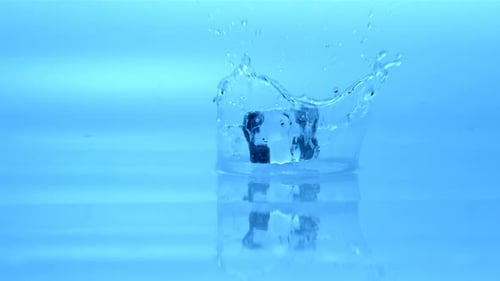 Clear Ice Cube Splashing Into Water on Blue Background