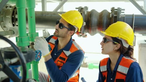 Professional male and female engineers in safety vests inspect industrial green pipes and valves