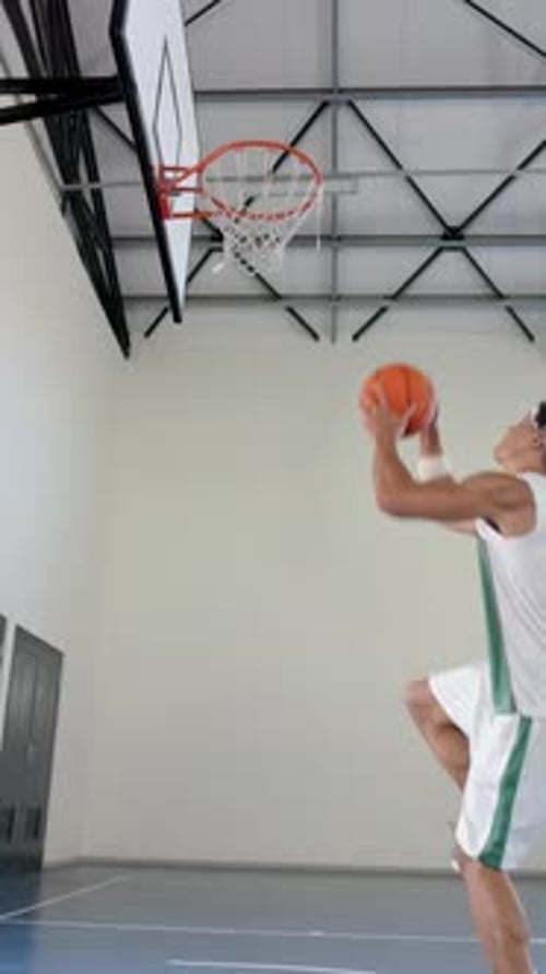 Vertical video: Playing basketball, male athlete jumping to score basket in gymnasium