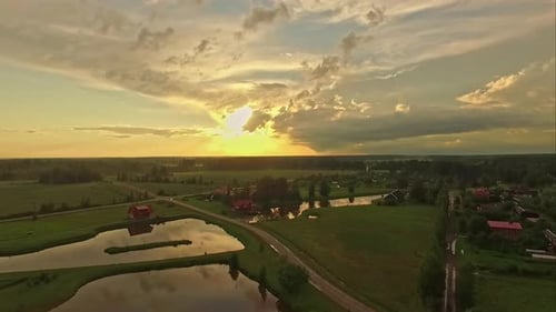 Aerial drone tilt up shot over village houses beside ponds and grasslands on a sunny morning.