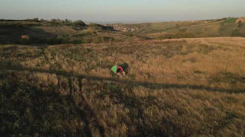 Two women camping at top of the hill sitting in front of the tent.