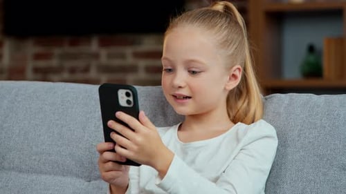 Cute girl using smartphone at home on sofa