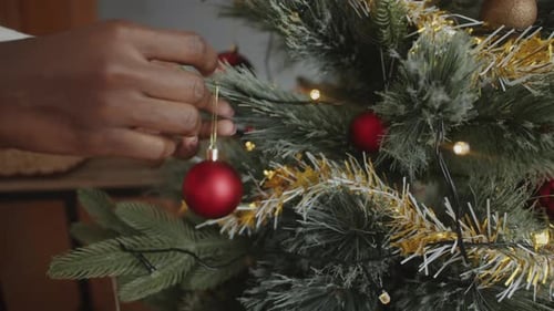 Hands Decorating Christmas Tree with Red Ornament