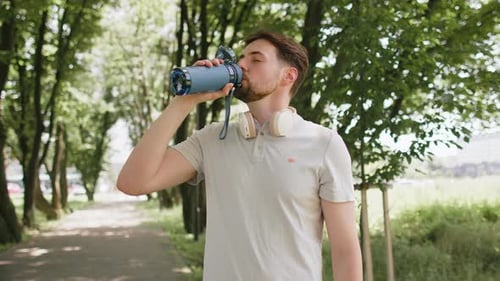 Sporty Athletic Thirsty Man Runner Jogger Drinking Water After Sport Workout in Park Outdoors