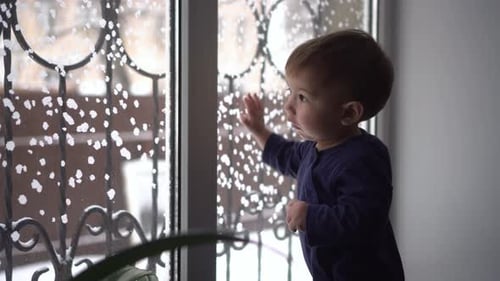 A Small Child Stands on the Windowsill and Looks Out the Window