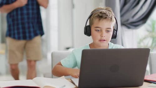 Glücklicher kaukasischer Junge sitzt am Tisch und benutzt Laptop für Online-Unterricht, Zeitlupe