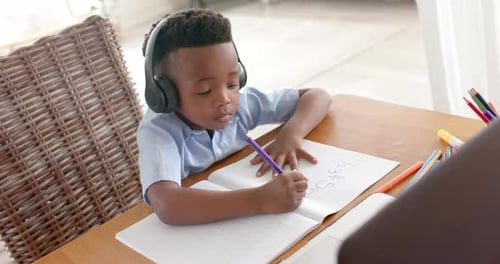 Boy with Headphones Writing in Notebook at Desk