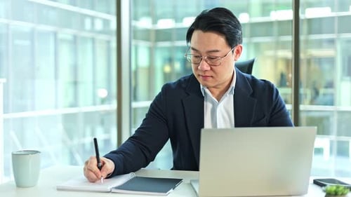 Korean Businessman Taking Notes While Working on Laptop in Office