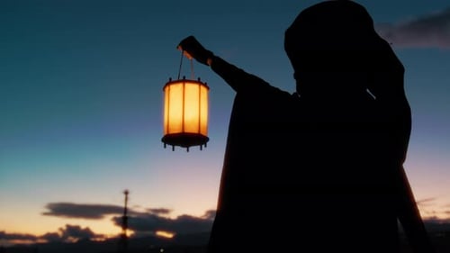 Silhouette Of A Mysterious Man With Cloak And Light Lantern At Sunset Sky