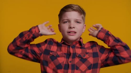 Niño gritando con las orejas cerradas usando las manos sobre fondo amarillo