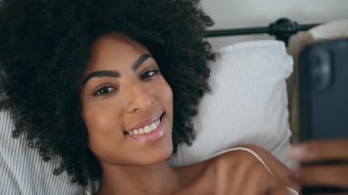 Woman Lies in Bed, Smiling While Using Phone