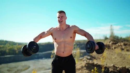 Muscular Man Working Out with Dumbbells Outdoors