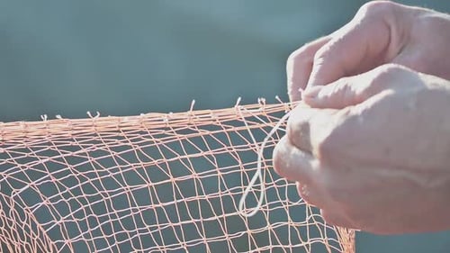 Hände eines Fischers, der ein zerrissenes Netz repariert