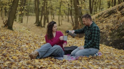 Ein Mann gießt Tee für eine Frau bei einem Picknick in einem Herbstwald ein