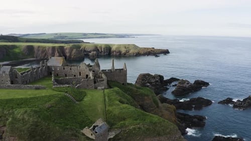 Drone shot pulling away from Dunnottar Castle on Scotland's rocky coastline.