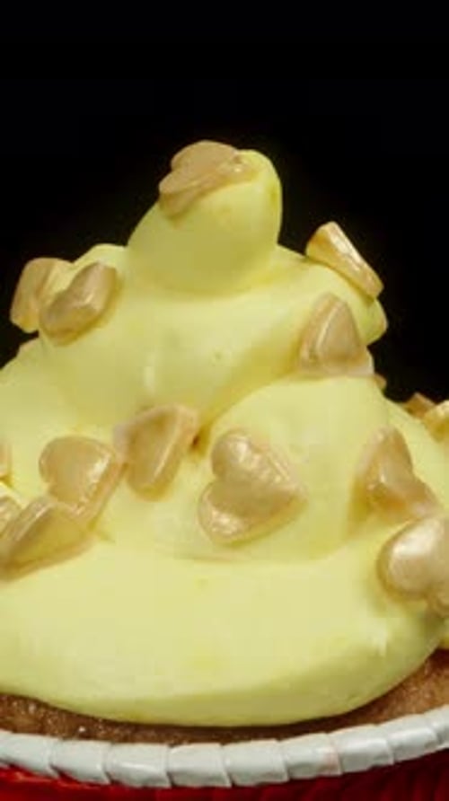 A cupcake with yellow frosting and golden sugar hearts on it. Dolly slider, close up.