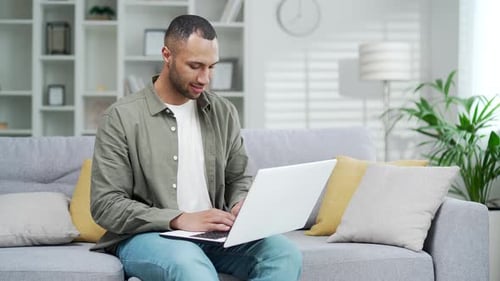 Man Comfortably Using Laptop on Gray Sofa at Home