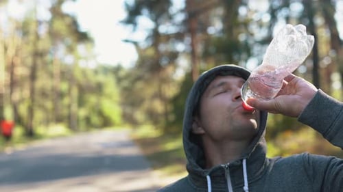 a Man in the Forest or in the Park Drinks Water From a Plastic Waste Bottle After a Hard Jogging