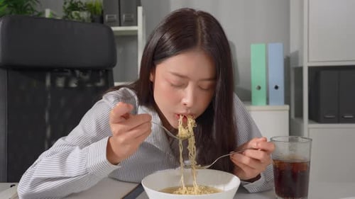Asian young businesswoman eating noodles while working in the office.