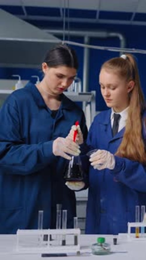 Young Female Scientists Collaborating in Modern Laboratory While Examining Dark Chemical Solution in