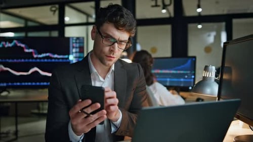Stock trader holding smartphone checks exchange market statistics online at workplace