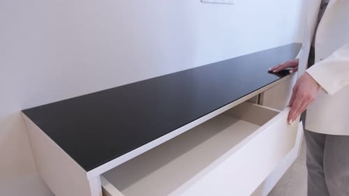 Girl opens a drawer in a wooden chest of drawers with tinted glass on top