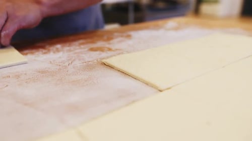 Bäcker schneidet Teig mit Pizzamesser auf Tisch in Bäckerei Closeup