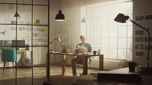 Frustrated and Tired Young Creative Designer Works on Laptop at His Desk, He Browses Through Concep