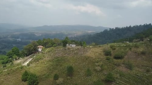 Beautiful landscape drone shot with blue skies, green crops and field and a house in top of a mounta
