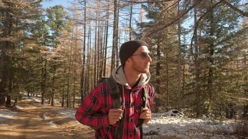 A Young Guy with a Backpack in the Hat Traveller Hipster Standing in the Woods Hiking ForestJourney