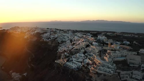 Oia Santorini island sunset drone shot overlooking white buildings and the sea, Greece in 4K