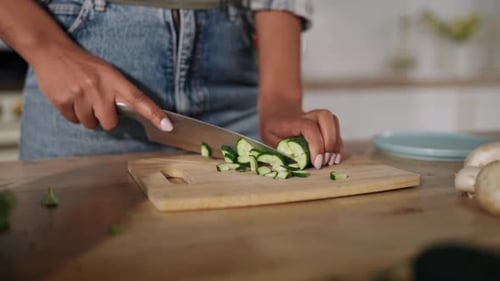 Woman Slicing Cucumber on Cutting Board in Kitchen