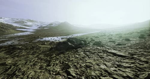 Expansive Rocky Landscape Under a Pale Sky with Distant Snow Covered Peaks
