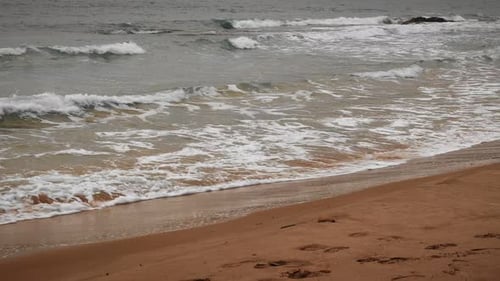 Sea waves crashing on sandy beach, creating white foam