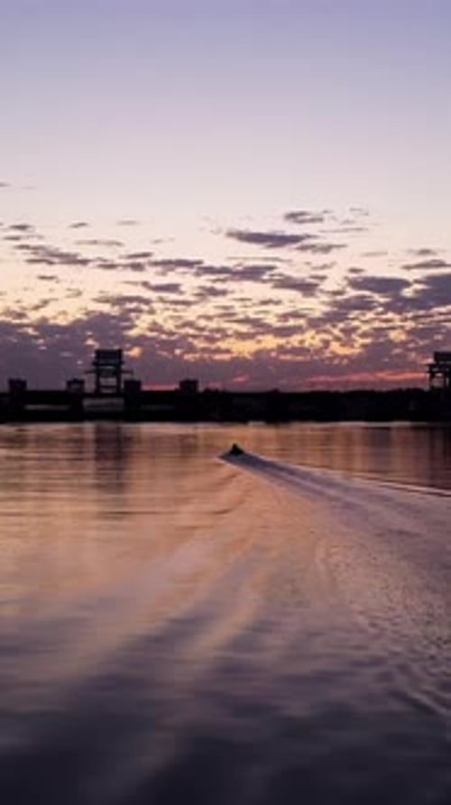 Reflet d'un coucher de soleil orange dans l'eau d'un lac urbain, images d'une silhouette sombre d'arbres qui poussent