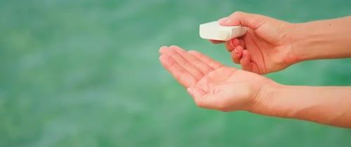 Frau hält ein weißes Glas, ein Kosmetikprodukt, in den Händen und lässt Lotion auf Meerwasser in ihre Handfläche fallen