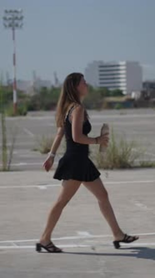 Young Girl Caucasian Woman in Short Black Dress Walking in Profile in an Industrial Area on the