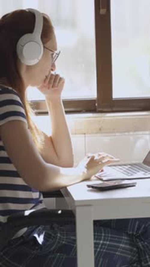 Woman Puts on Headphones and Uses Laptop Indoors