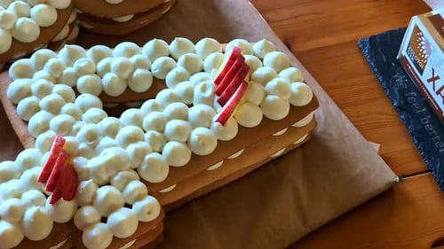 Close-up of pastry chef person's hands placing strawberry apple fruit onto number 4 four letter cake