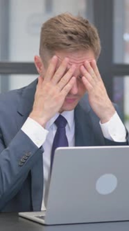 Stressed Businessman Working at Laptop Suffering from Headache